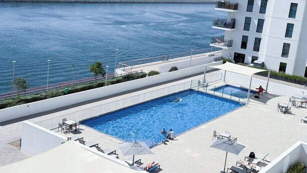 A rooftop pool with a view of the sea, surrounded by lounge chairs and umbrellas. - Yas Island Waters Edge Studio (Abu Dhabi)