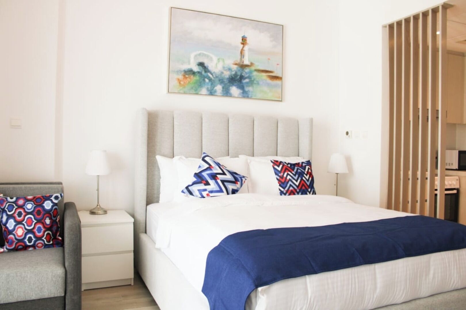 A bedroom with a bed, two bedside tables, a chair, a painting, and a wardrobe.
