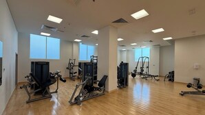 A spacious gym with multiple exercise machines, large windows, and a wooden floor. - Yas Island Waters Edge Studio (Abu Dhabi)