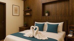 Habitación de hotel con cama, mesita de noche, cabecera de madera, estante empotrado con plantas e imagen enmarcada.