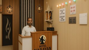 Un mostrador de recepción de hotel con un cartel que dice "HOTEL NARAYAN NIWAS". Hay luces decorativas, un cartel en la pared con los horarios de registro de entrada y salida, y un cartel que indica que no se admiten mascotas.