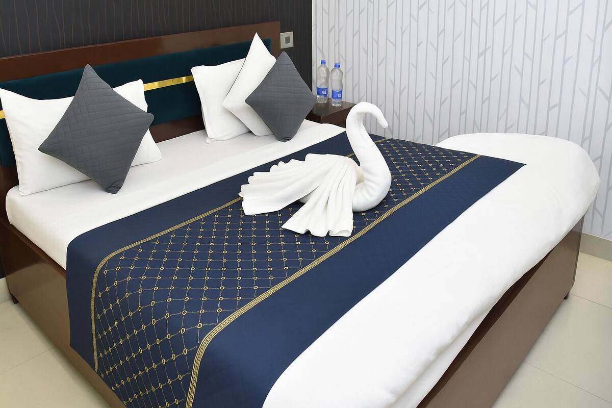 A neatly made bed with a blue and gold patterned bedspread, white pillows, and a white towel folded on the bed.