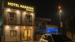Un hotel llamado "Hotel Narayan Niwas" con una entrada bien iluminada y un coche aparcado delante.