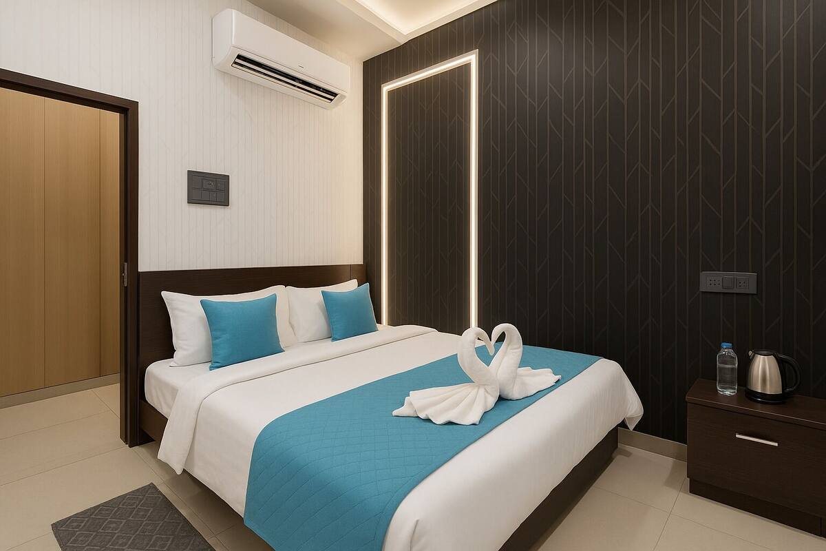 A modern hotel room with a neatly made bed, a bedside table with a kettle, and a wall-mounted air conditioner.