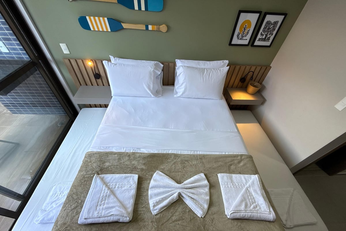 Una cama bien hecha con sábanas blancas, un edredón marrón y toallas dobladas.