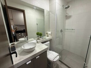Un baño moderno con un espejo grande, un lavamanos blanco, una cabina de ducha de vidrio y un inodoro.