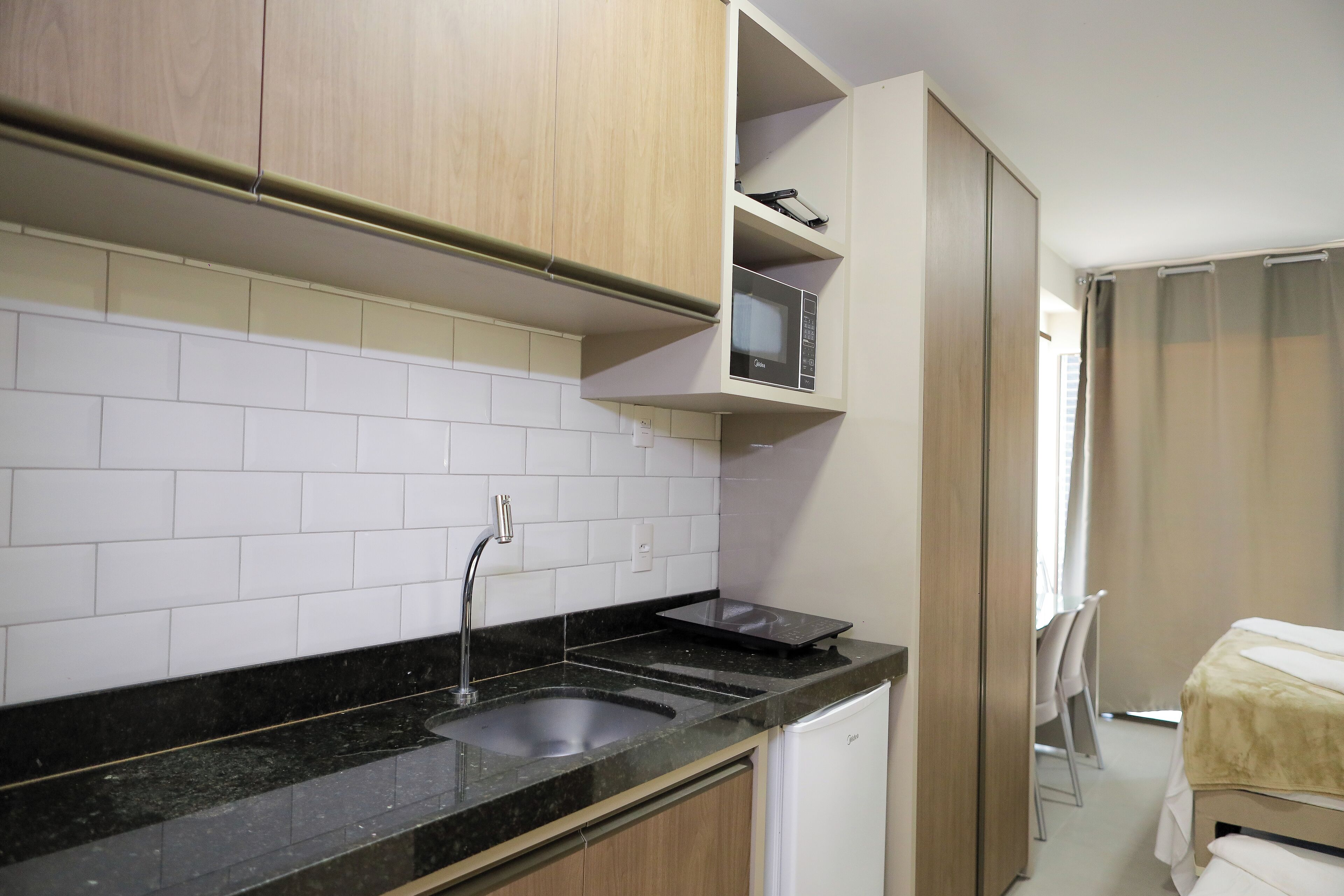 Cozinha compacta com bancada preta, azulejos brancos e armários de madeira.