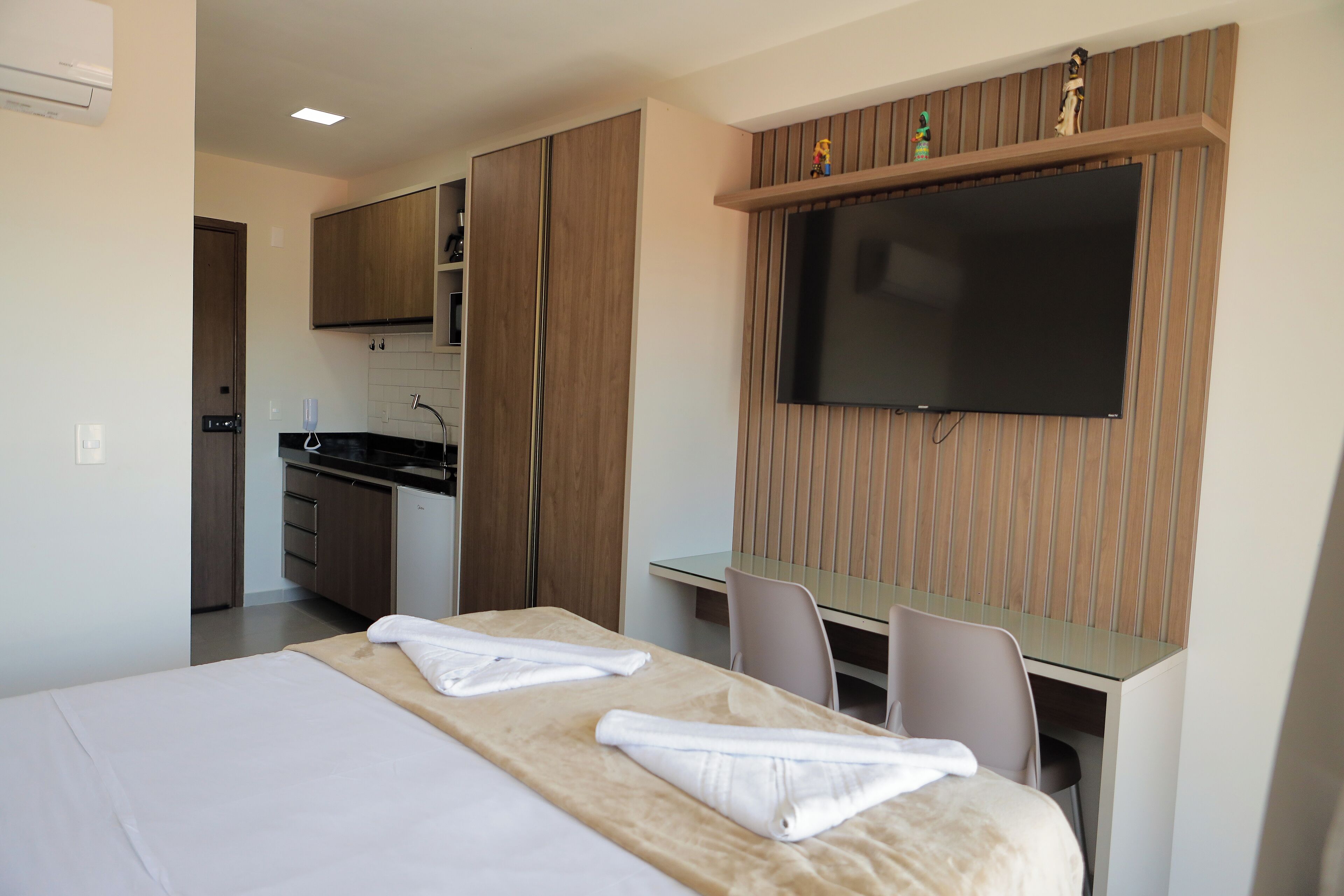 Una habitación de hotel con cama, escritorio, silla, televisor y kitchenette.