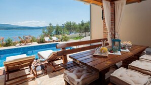 Une terrasse avec une piscine, des meubles en bois et une vue sur la mer.