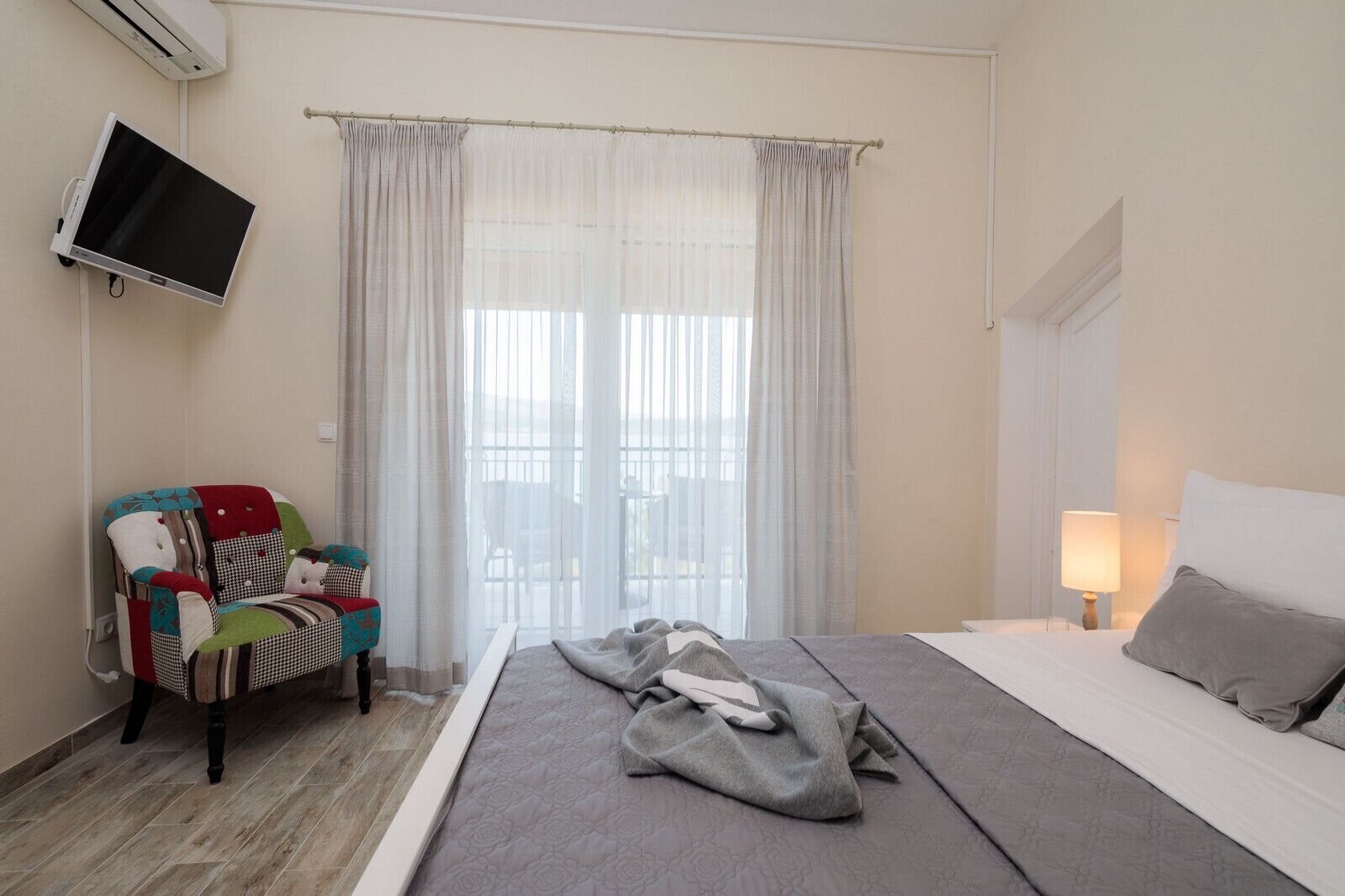 Ein Hotelzimmer mit einem Bett, einem Sessel, einem Wandfernseher und einem fenster mit Vorhängen.