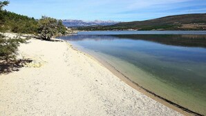 Une plage à l’eau claire, un rivage sablonneux et des montagnes en arrière-plan.