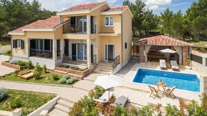 Une maison à deux étages avec une piscine, un espace salon extérieur et une terrasse couverte.