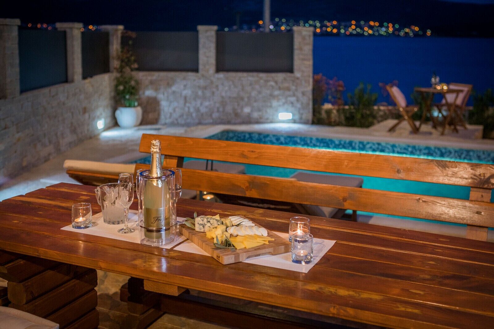 A wooden table with a bottle of champagne, glasses, and a cheese board.