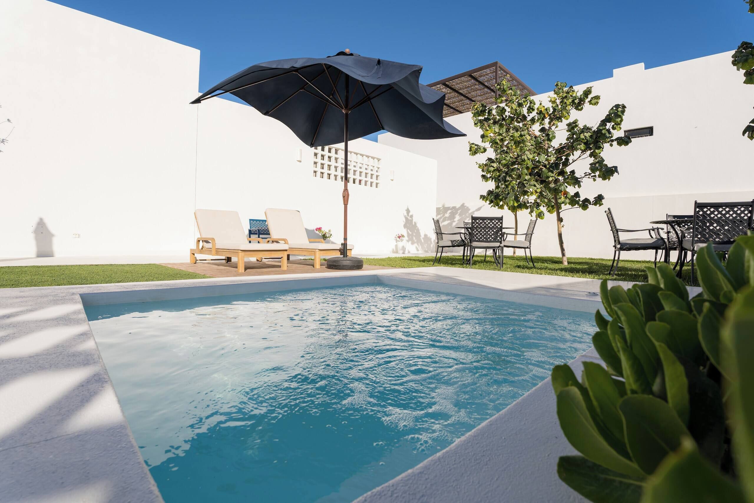 A swimming pool with lounge chairs and umbrellas, surrounded by white walls and greenery.