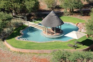 A swimming pool with a thatched-roof pavilion, a wooden bridge, and lounge chairs. - Mattanu Private Game Reserve (Dikgatlong)