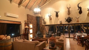 A cozy living room with sofas, a fireplace, and mounted animal heads on the wall. - Mattanu Private Game Reserve (Dikgatlong)