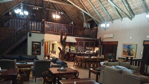 A spacious lounge with wooden furniture, a staircase, and a bar area. - Mattanu Private Game Reserve (Dikgatlong)
