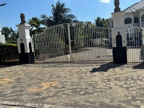 A gated entrance with a metal gate, a paved driveway, and a building with a tiled roof. - Choose Your Stay: Private Guest Rooms, Bathroom, or a Furnished Apartment (Clarendon Park)