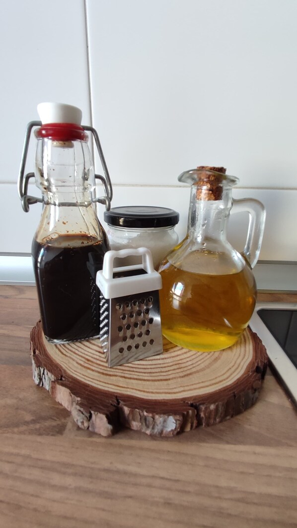 A wooden cutting board with a bottle of dark liquid, a bottle of light yellow liquid, and a metal grater. - Charming, with views, comfortable and centrally located. Close to the river and the National Park. (Boltaña)