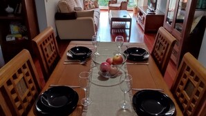 Een eetgedeelte met een houten tafel gedekt voor twee personen, een fruitschaal en een hanglamp.