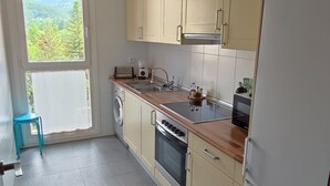 Een moderne keuken met beige kastjes, een roestvrijstalen spoelbak en een inbouwoven. Een groot raam biedt uitzicht op groen.
