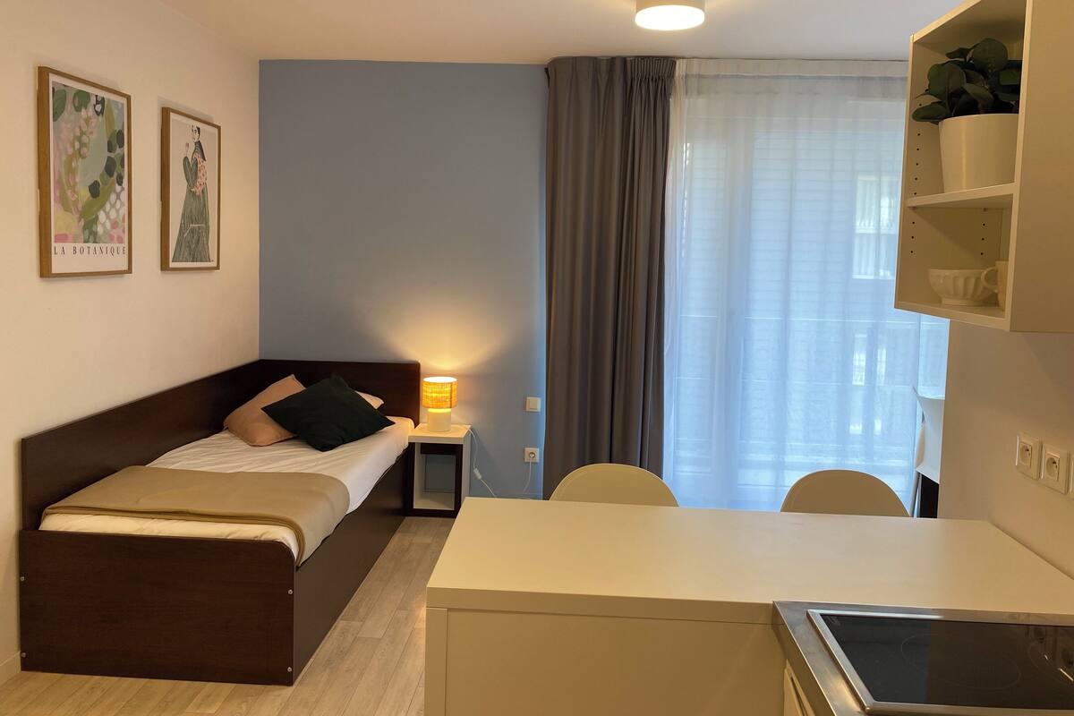 Un dormitorio con cama, mesita de noche, lámpara y escritorio con silla. Hay dos cuadros en la pared.