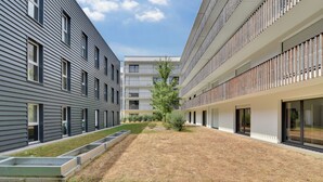 Un bâtiment moderne doté d’une cour intérieure, comprenant un mélange d’espaces résidentiels et commerciaux, ainsi que des balcons et de grandes fenêtres.