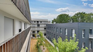 Un bâtiment moderne doté d’une cour intérieure, avec un mélange de balcons et de fenêtres, et un ciel dégagé.