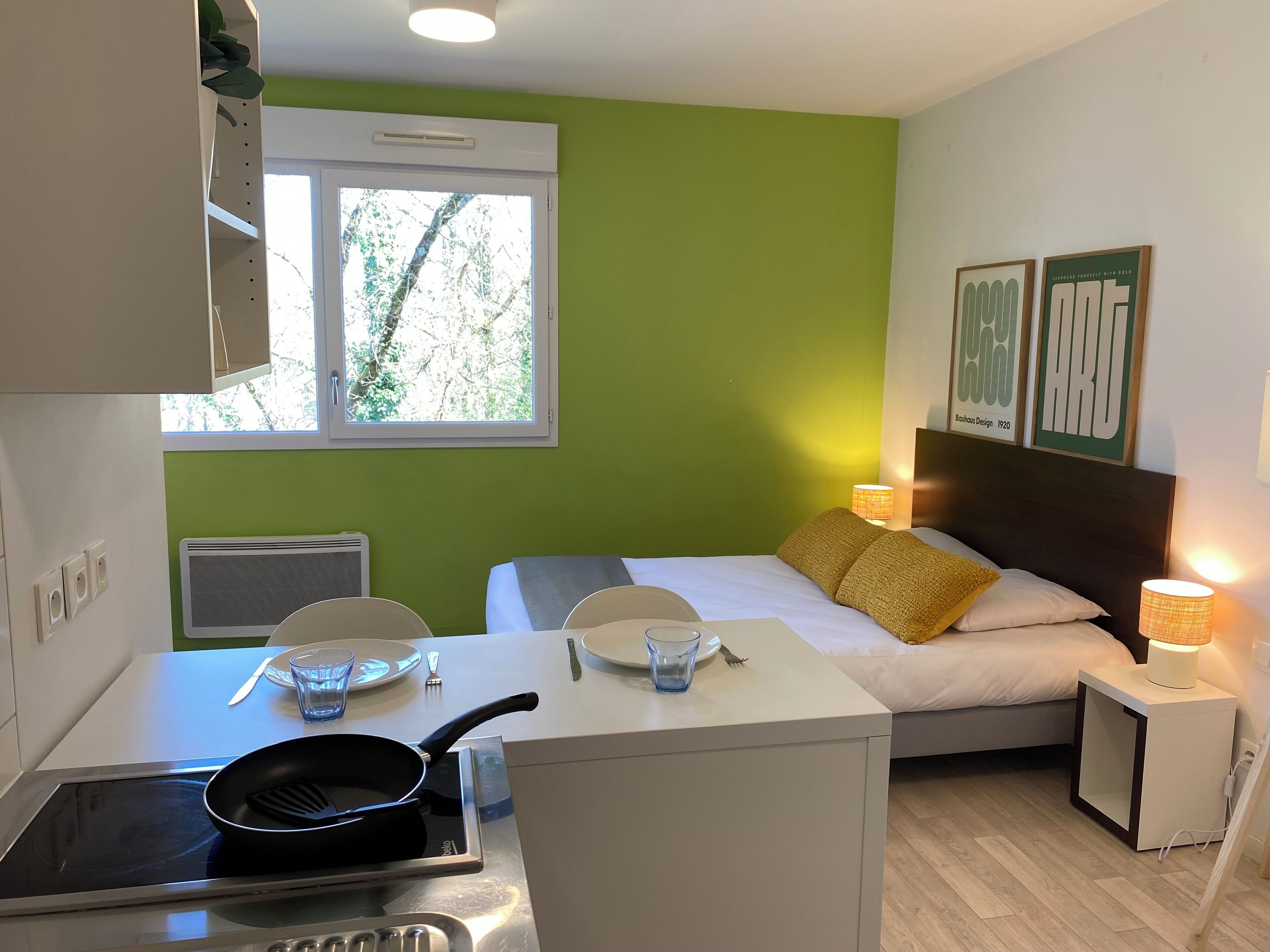 Una stanza compatta con un letto, un comodino e un angolo cottura.