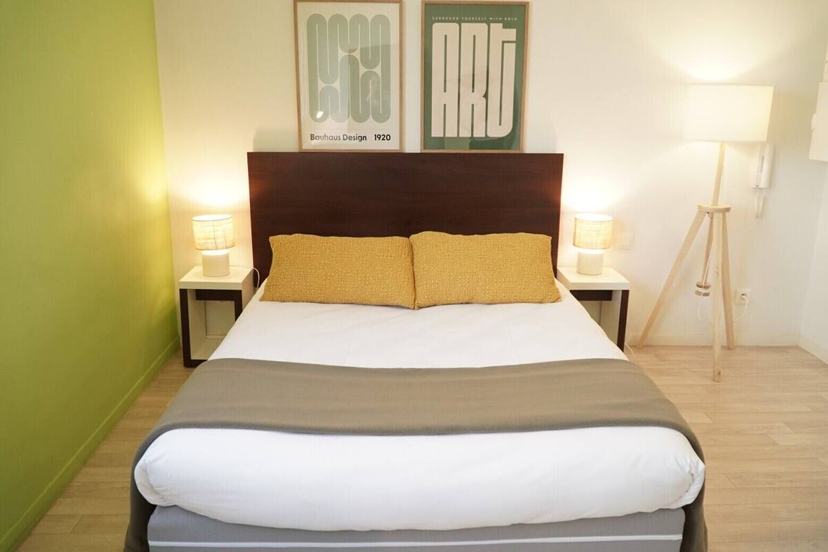 Una habitación de hotel con una cama grande, dos lámparas de noche, un cuadro enmarcado sobre la cama y una lámpara de pie en la esquina.