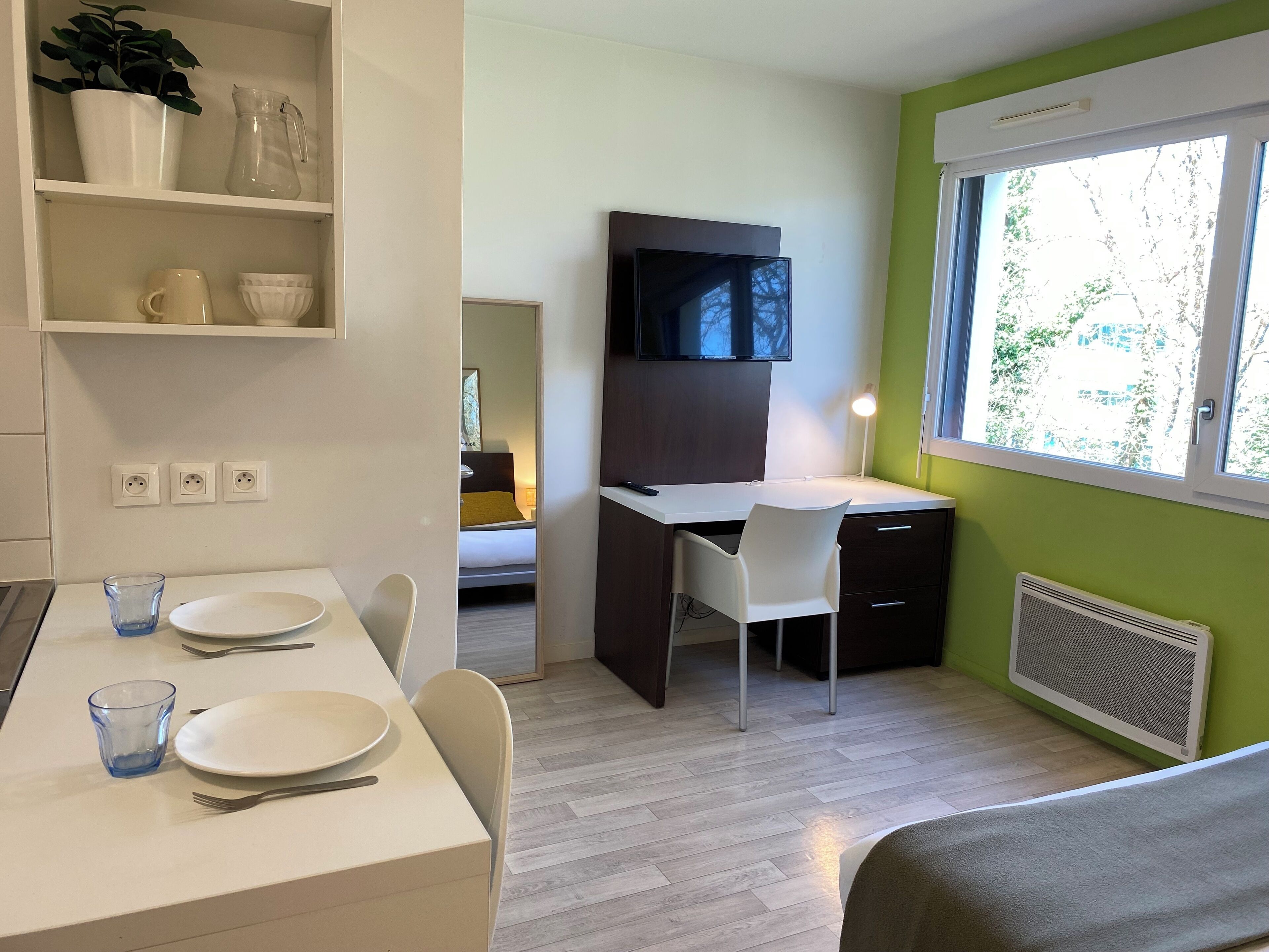 Ein kompaktes Hotelzimmer mit Essbereich, Schreibtisch, Bett und großem Fenster.
