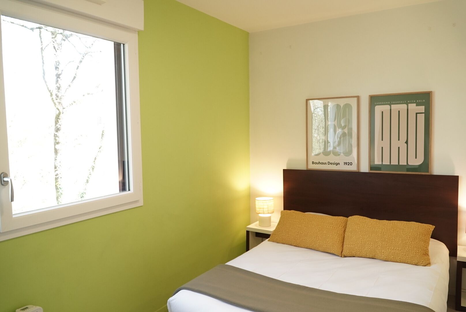 Une chambre à coucher avec un lit, une table de chevet, une lampe et deux tableaux encadrés accrochés au mur.
