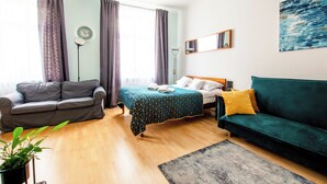 A room with a bed, a green sofa, a grey sofa, a wooden floor, and a potted plant. - Luxury European Apartment (Kraków)