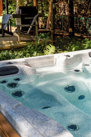 A hot tub with multiple jets, surrounded by a wooden deck and lush greenery.