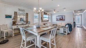A spacious living room with a large wooden dining table, white upholstered chairs, a beige sofa, and a blue throw blanket. - EXPERIENCE RESORT-STYLE LIVING IN THE HEART OF NAPLES RESERVE (Naples)