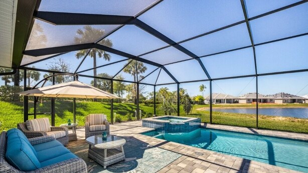 A covered outdoor area with a pool, seating, and a view of a lake. - EXPERIENCE RESORT-STYLE LIVING IN THE HEART OF NAPLES RESERVE (Naples)