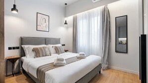 Ein modernes Schlafzimmer mit einem großen Bett, Nachttischen, einer Wand-Klimaanlage und einem Fenster mit Vorhängen.