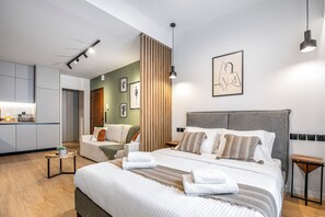 A modern hotel room with a large bed, a sitting area with a sofa, a small round table, and a kitchenette in the background. - Avia Deluxe Studio- Athens Modern Escape (Athens)