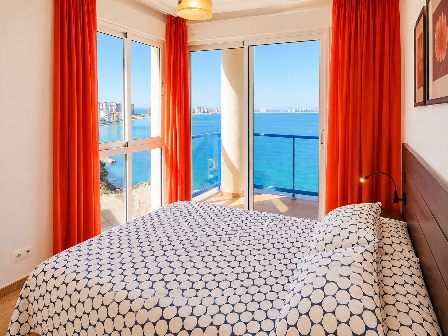 Une chambre à coucher avec un lit, une vue sur la mer et un balcon agrémenté de rideaux rouges.