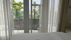A hotel room with a bed, a view of the outdoors through sheer curtains, and a balcony with a patterned railing. - Royal Apartment (Michamvi)