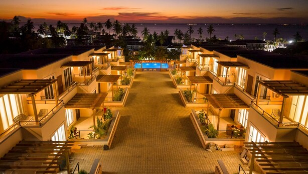 A resort with multiple balconies, a central pool, and a view of the ocean at sunset. - Royal Apartment (Michamvi)