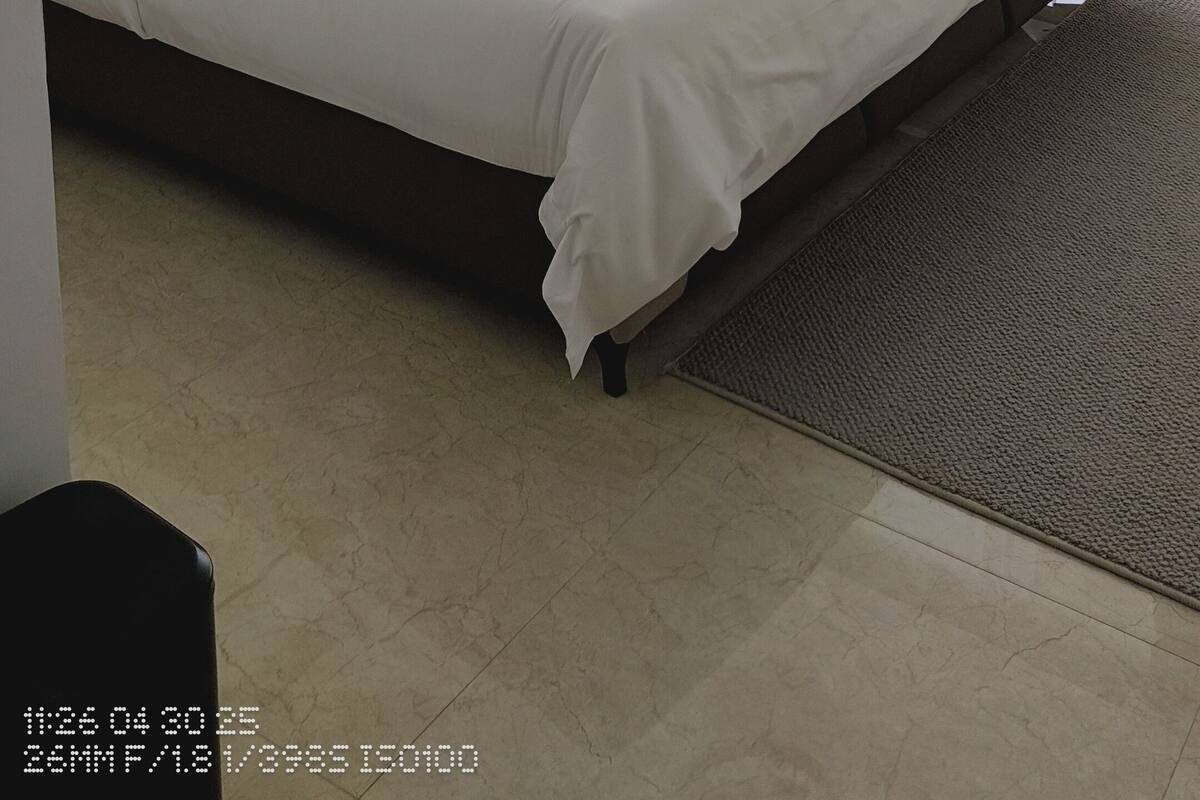 A neatly made bed with a swan-shaped pillow, a bedside lamp, and a view of the outside through sheer curtains.