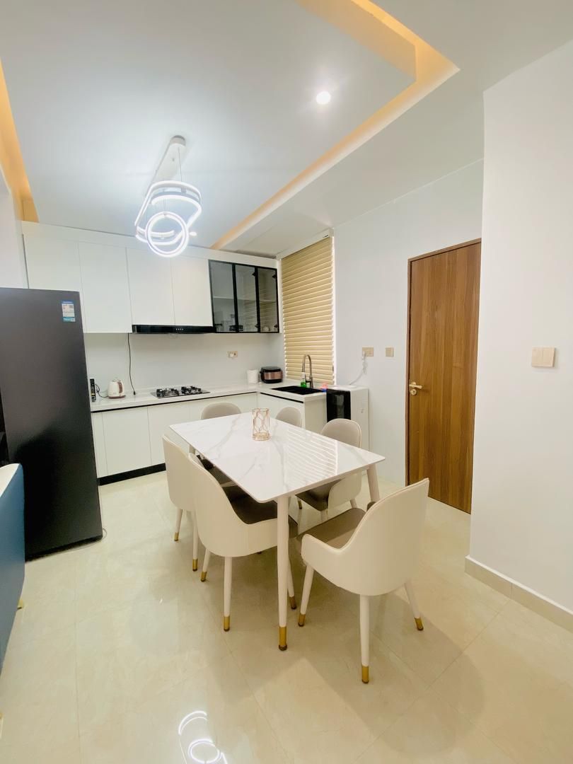 A modern kitchen with white cabinets, a black refrigerator, and a dining table with white chairs.