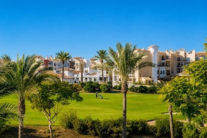 Campo de golf con palmeras y un complejo de edificios al fondo.