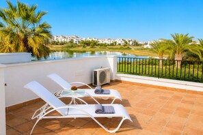 A terrace with two white lounge chairs, a small table with a flower, and an air conditioning unit.