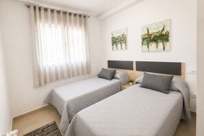 Una camera d'albergo con due letti, una finestra con tende leggere e due quadri astratti alle pareti.