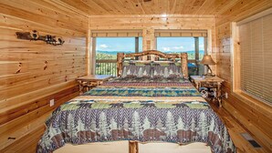 A wooden cabin bedroom with a bed, nightstands, and a large window offering a view of the outdoors. - Wild Honey- 4bdrm, Incredible Mtn Views, Pool Table, Fire Pit, Pool Access (Sevierville)
