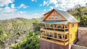 Eine zweistöckige Holzhütte mit einem Balkon, umgeben von bewaldeten Hügeln.