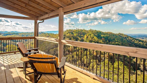 Une terrasse en bois avec deux fauteuils Adirondack et un baril, offrant une vue sur un paysage boisé sous un ciel dégagé.