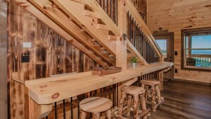 Un intérieur en bois avec un escalier en bois, un comptoir de bar en bois avec des tabourets, et une vue par une fenêtre.